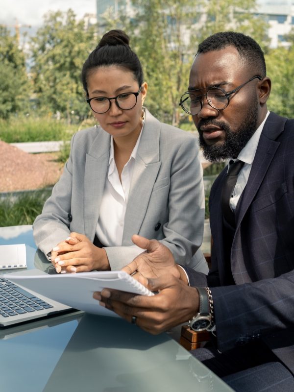African businessman showing paper to Asian female business partner at outdoor meeting